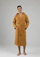 Man wearing a mustard yellow turkish waffle robe on a gray background