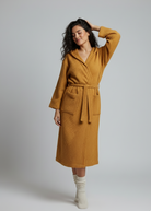 Woman wearing a mustard yellow waffle robe against a plain background